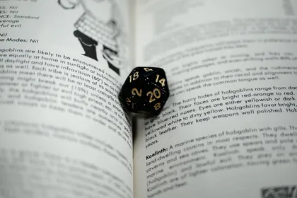 A black twenty-sided die resting in the gutter of an open rulebook, the page describing hobgoblins