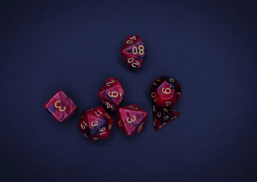 A seven-dice polyhedral set in swirled red and purple, laid out on dark blue felt